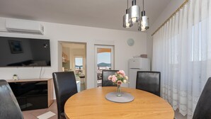 Ett modernt vardagsrum med ett runt matbord i trä, svarta läderstolar, en platt-TV och utsikt över utomhusmiljön genom en dörr.