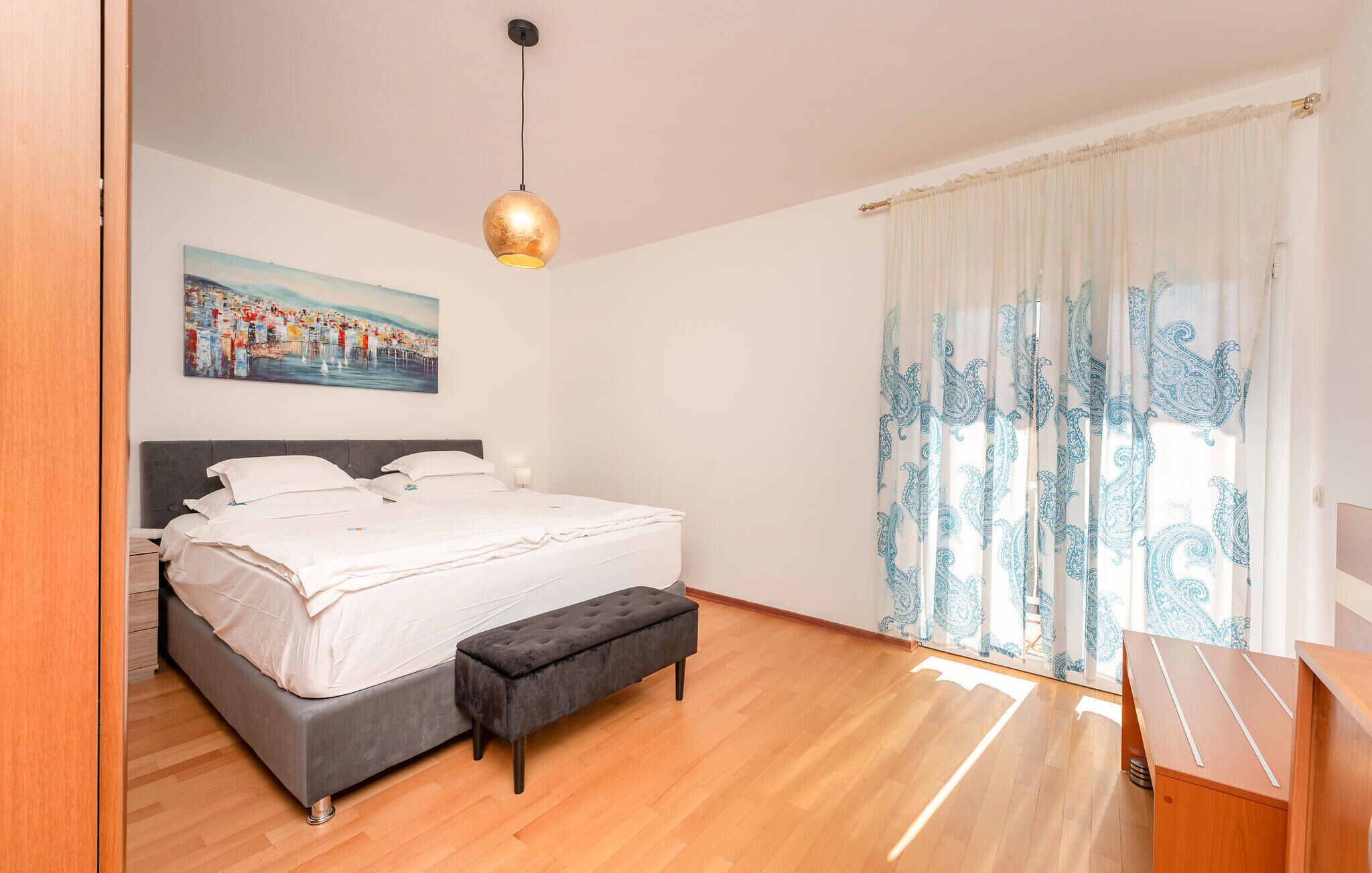 Un dormitorio con una cama, un banco, un cuadro y una lámpara colgante.