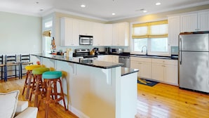 A modern kitchen with white cabinets, stainless steel appliances, and a central island with stools. - The Willis: Dog Friendly, Ocean/Sound View Condo, Near Beach (Atlantic Beach)