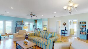 A spacious living room with a striped sofa, a wooden coffee table, and a chandelier. - The Willis: Dog Friendly, Ocean/Sound View Condo, Near Beach (Atlantic Beach)