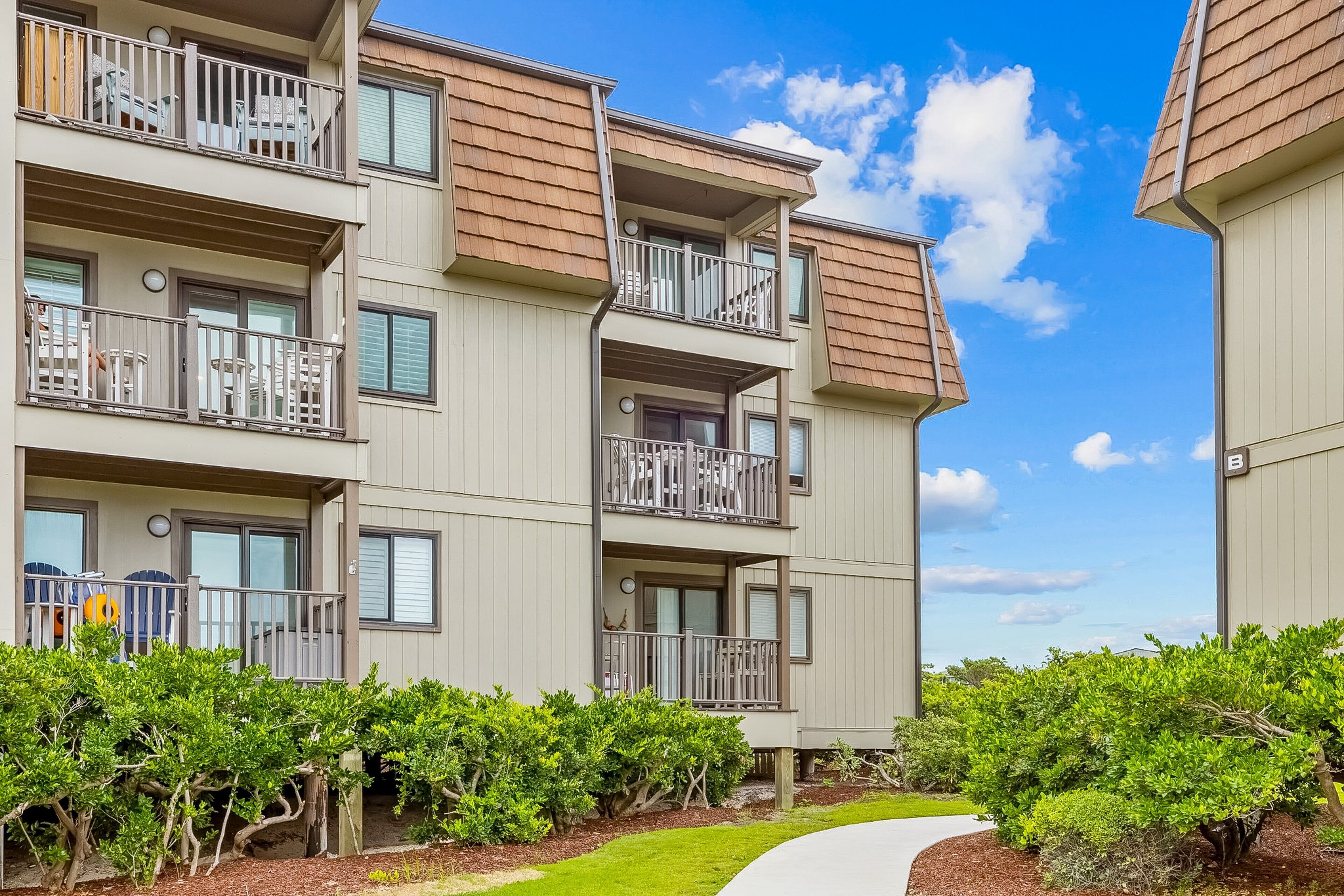 A multi-story residential building with balconies, a pathway, and well-maintained landscaping.