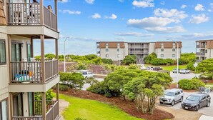 A residential building with a balcony, a parking area, and surrounding greenery. - Cheery coastal condo with balcony, AC, W/D, 2 pools, grills, & beach access (Atlantic Beach)