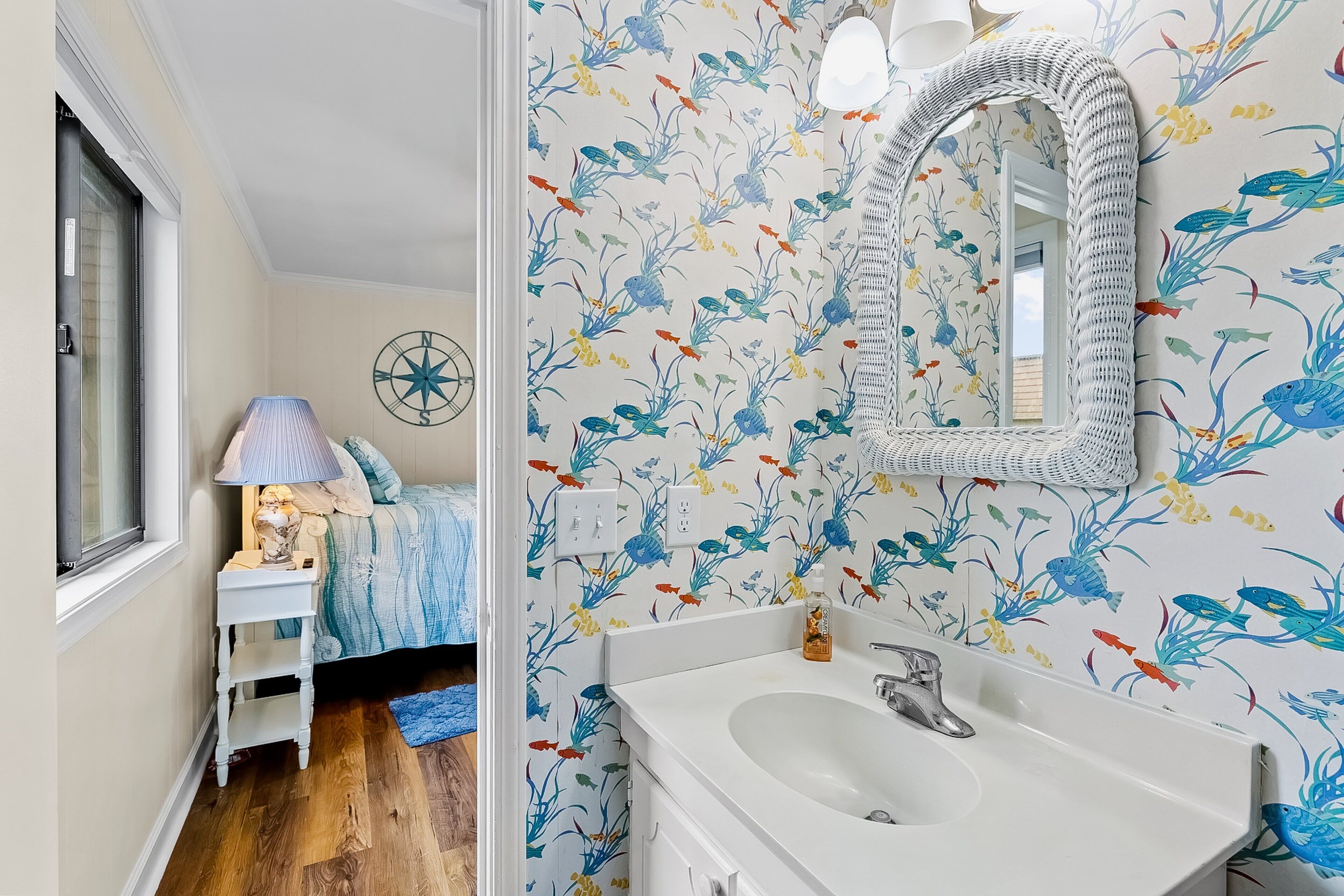 A bathroom with a white sink, a mirror, and a fish-patterned wallpaper.