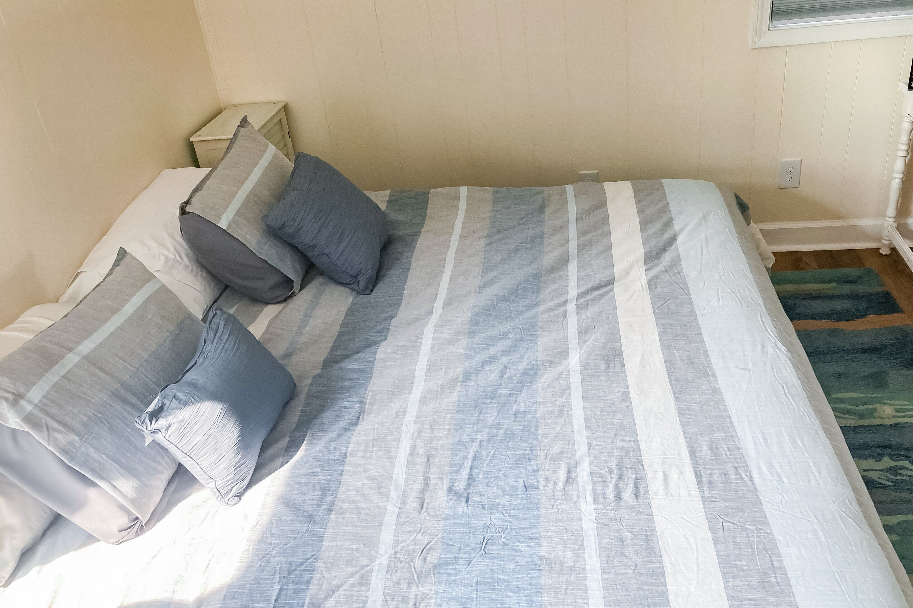 A bed with striped bedding and two pillows, a nightstand, and a power outlet on the wall.