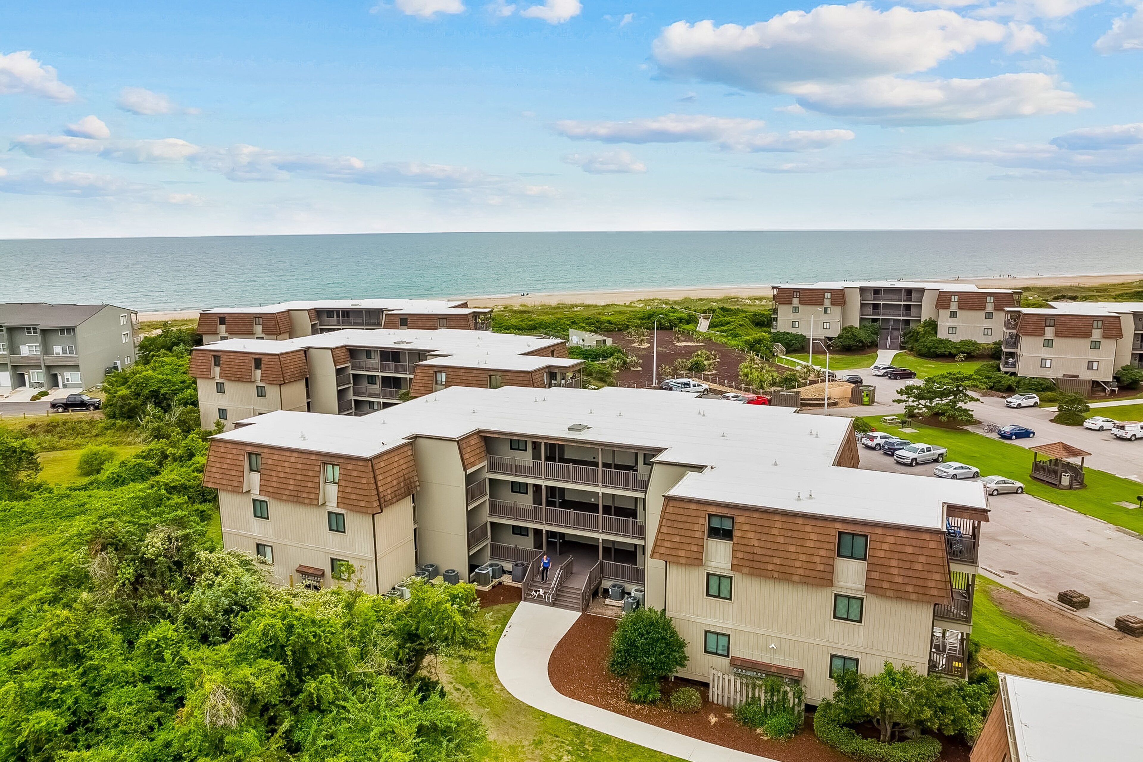 A multi-story residential building with a curved driveway, a parking area, and a view of the beach.