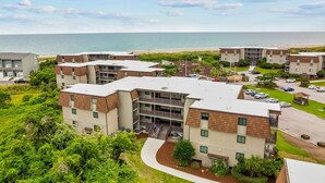 A multi-story residential building with a curved driveway, a parking area, and a view of the beach. - Cheery coastal condo with balcony, AC, W/D, 2 pools, grills, & beach access (Atlantic Beach)