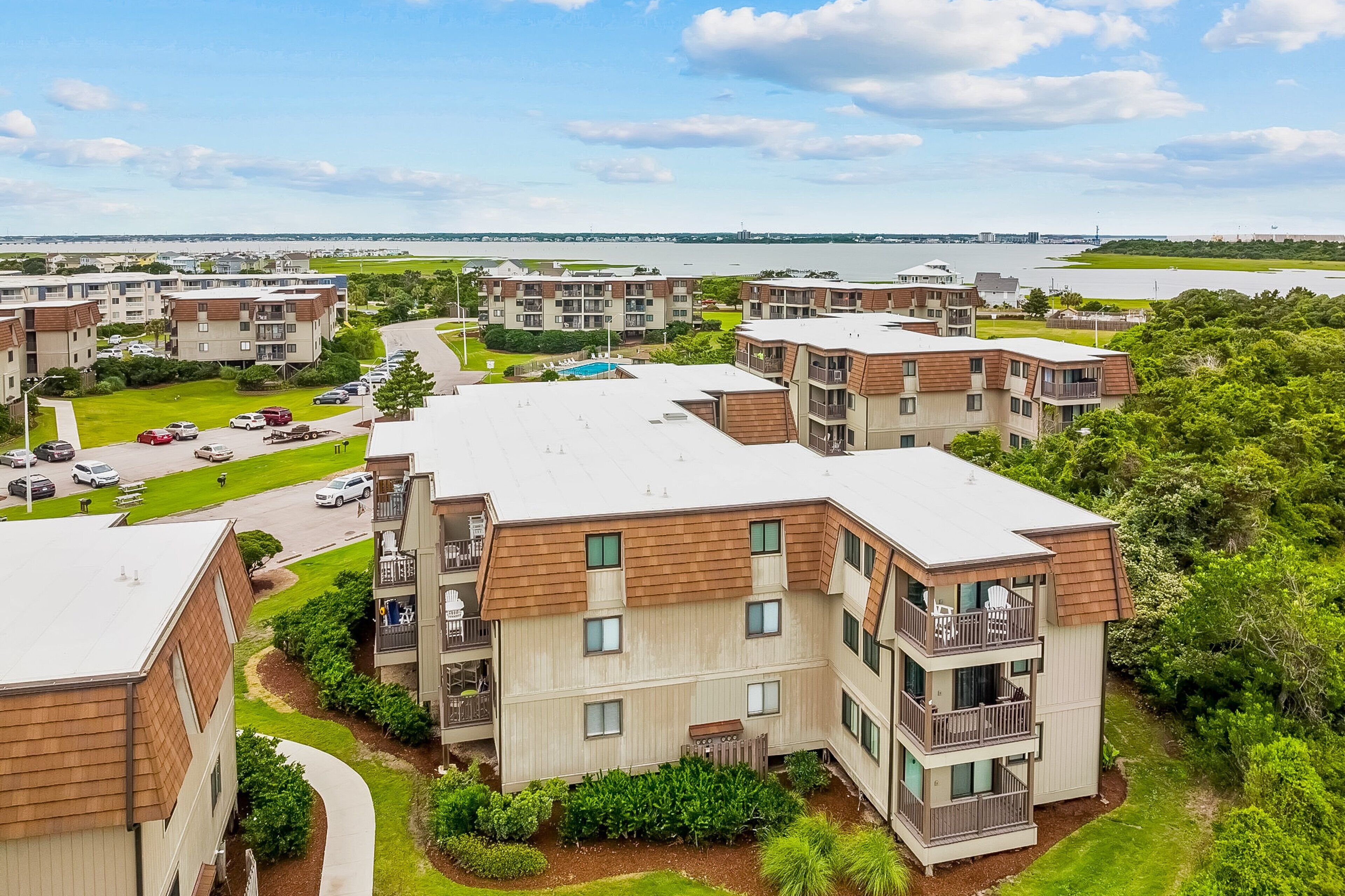 A residential complex with multiple apartment buildings, a parking area, and a view of a body of water.