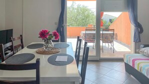 Un comedor con una mesa, sillas y un florero. Hay una puerta corrediza de vidrio que da a un patio exterior con una mesa y sillas.