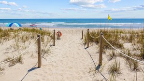 A sandy beach path leading to the ocean with a lifeguard stand and a yellow flag. - Dog-friendly home with ocean/sound views and private beach path (Pine Knoll Shores)