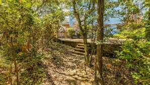 A pathway leading through a wooded area with a view of a house in the background. - Dog-friendly home with ocean/sound views and private beach path (Pine Knoll Shores)