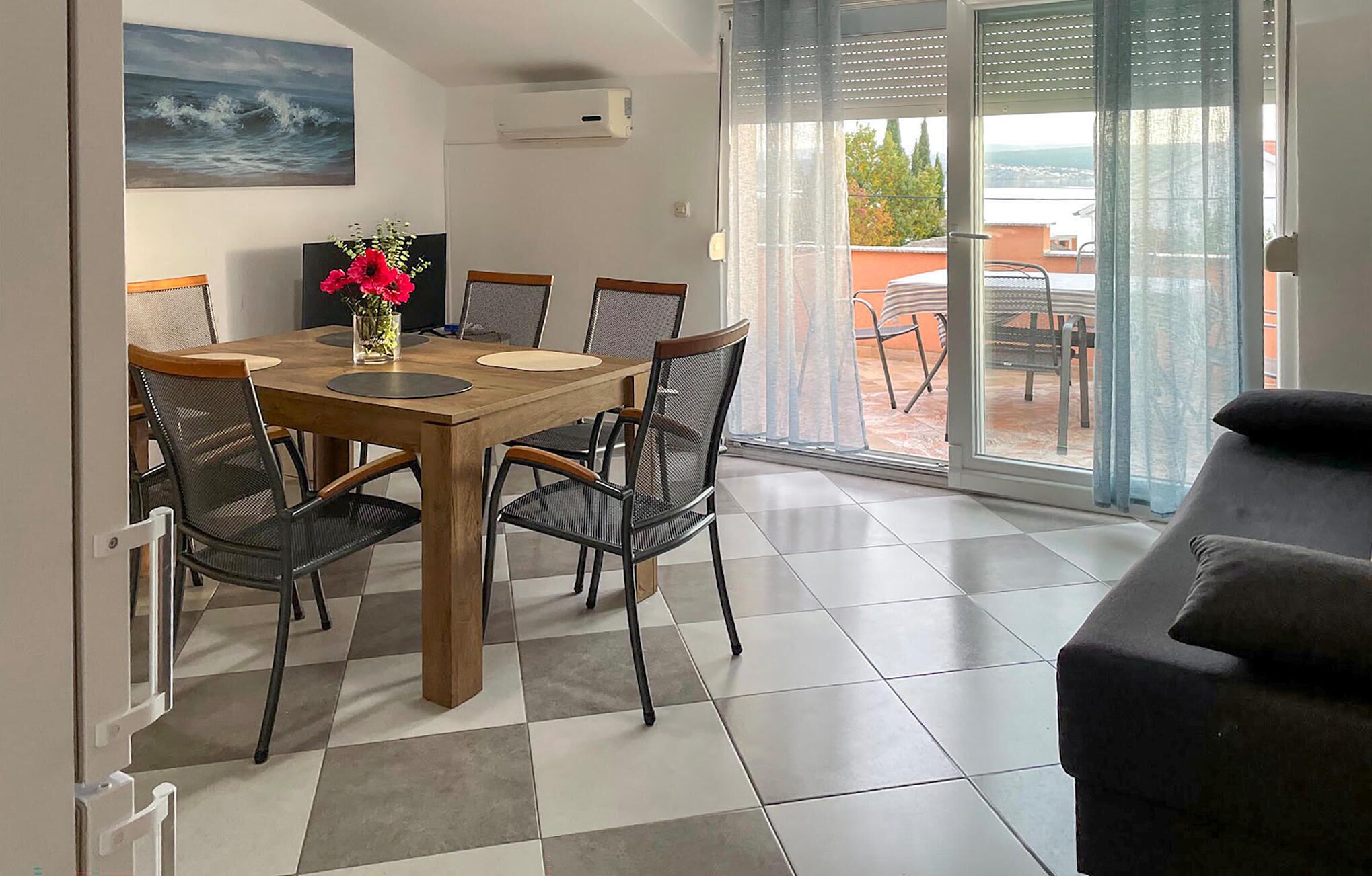 Ein Essbereich mit Holztisch und Stühlen, einer Blumenvase und Blick ins Freie durch eine Glastür.