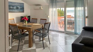 Un coin repas avec une table et des chaises en bois, un vase de fleurs et une vue sur l’extérieur grâce à une porte vitrée.
