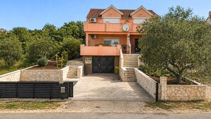 Une maison à deux étages avec une façade en pierre, un portail noir et un escalier menant à l’entrée.