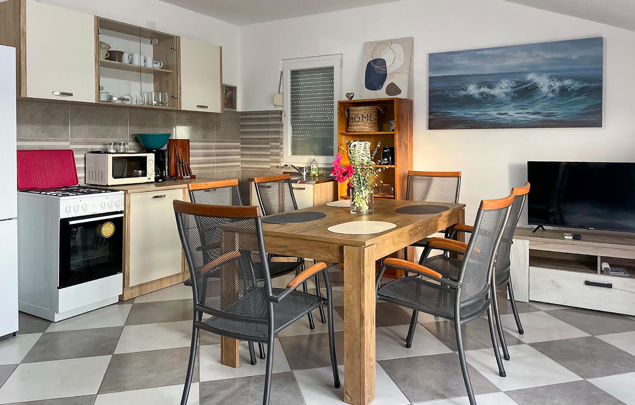 Eine moderne Küche mit Essbereich, ausgestattet mit einem Holztisch, Stühlen, einem Fernseher und einem Gemälde vom Meer.
