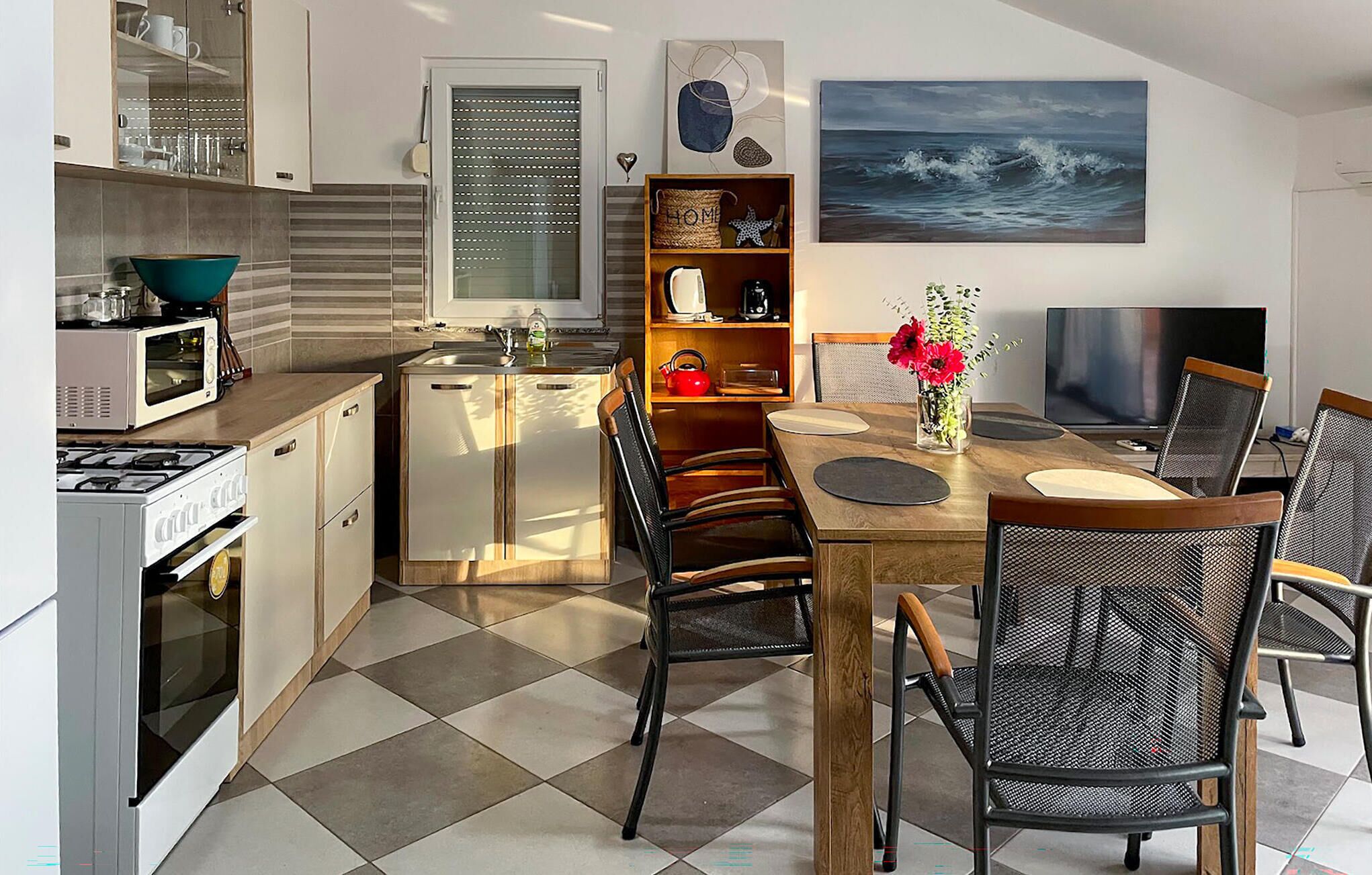 A compact kitchen with a microwave, stove, and sink. There is a dining area with a table, chairs, and a TV.