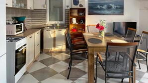 Une cuisine compacte équipée d’un four à micro-ondes, d’une cuisinière et d’un évier. Un coin repas est aménagé avec une table, des chaises et un téléviseur.