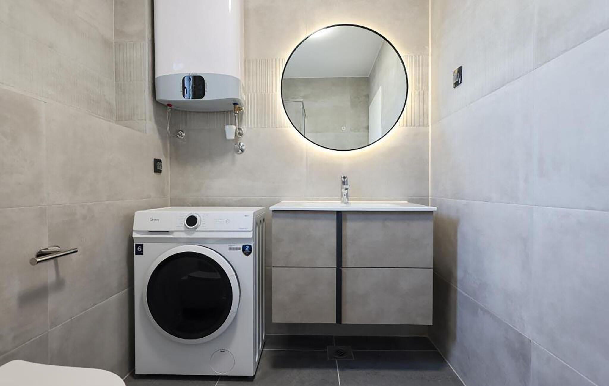 Een kleine badkamer met een geïntegreerde wasmachine en droger, een wastafel met spiegel en een toilet.