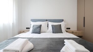 Un lit bien fait, avec une couette grise et blanche, deux oreillers et deux serviettes pliées posées sur le lit.