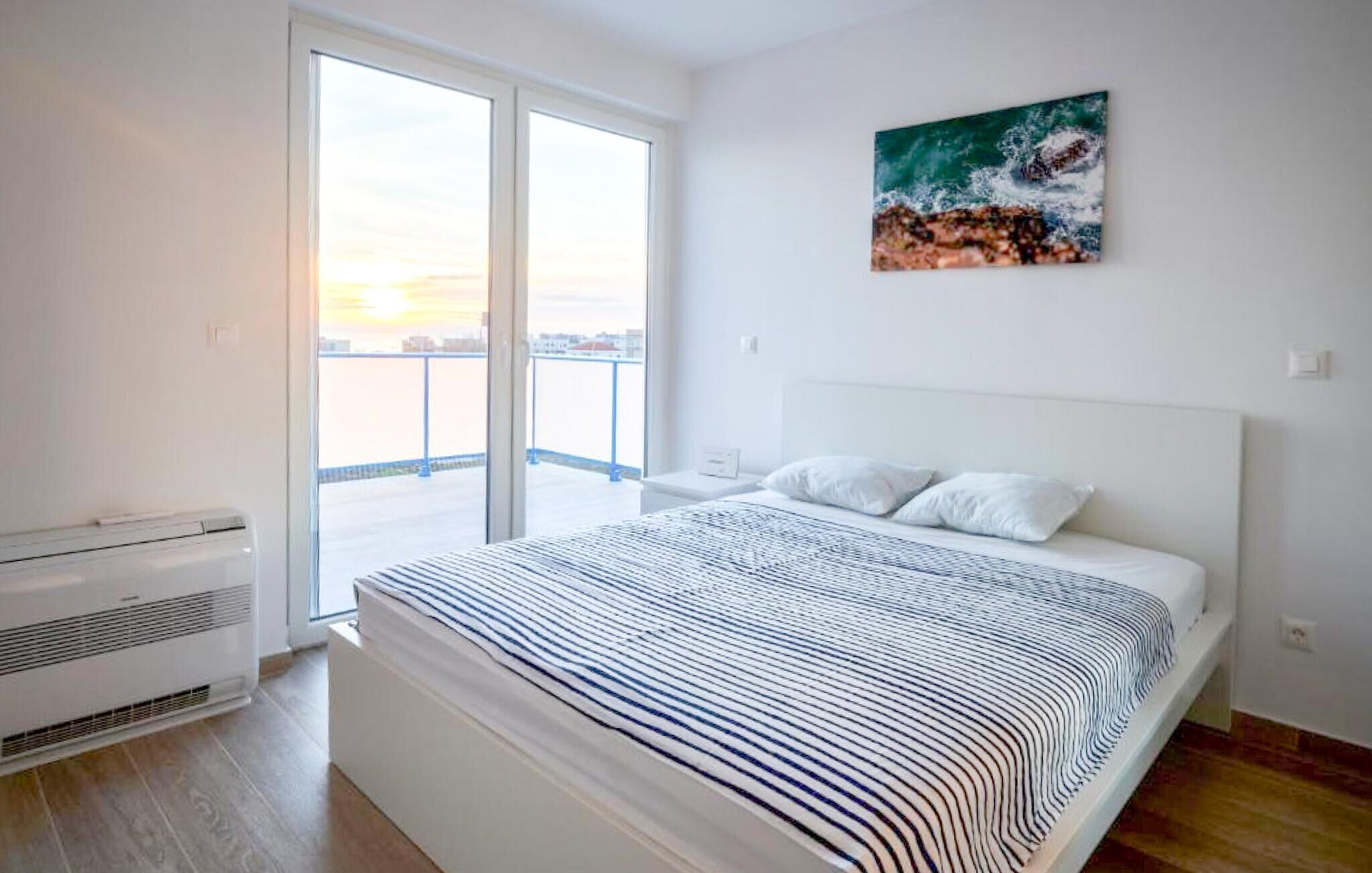 Un dormitorio moderno con una cama grande, vistas de la ciudad a través de una puerta corredera y un cuadro de una ola en la pared.