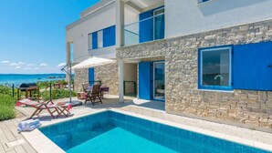 A modern building with a pool, outdoor seating, and a view of the sea.