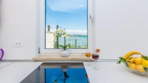 A kitchen with a view of the sea, a vase with flowers, and a fruit bowl.