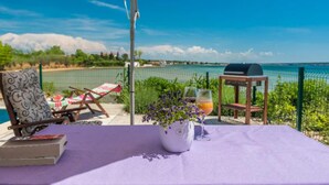 A patio with a table, chairs, a grill, and a view of the sea.