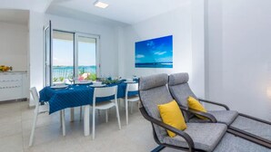 A modern dining area with a table set for two, a view of the sea through large windows, and a comfortable seating area with a chair. - Lovely home in Privlaka (Privlaka)