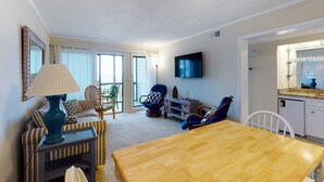 A living room with a wooden table, striped sofa, blue armchair, and a lamp. - 2nd-Floor Condo in Oceanfront Location w/WiFi, Screened-In Balcony, Shared Pool (Atlantic Beach)