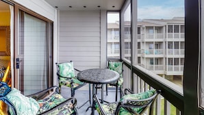 A balcony with a table and chairs, a sliding glass door, and a view of a multi-story building with balconies. - 2nd-Floor Condo in Oceanfront Location w/WiFi, Screened-In Balcony, Shared Pool (Atlantic Beach)