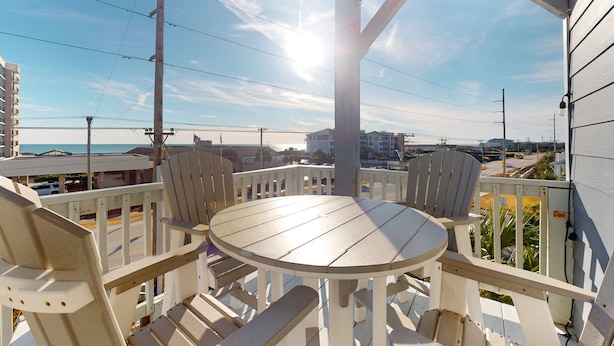 Ein Balkon mit rundem Tisch und vier Stühlen, mit Blick auf Strand und Gebäude.