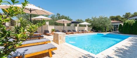 A poolside area with lounge chairs and umbrellas, a stone wall, and a clear blue pool.