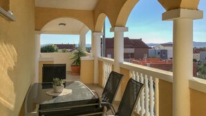 A balcony with a table and chairs, a potted plant, and a view of surrounding buildings.