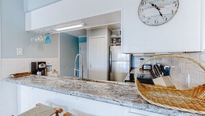 Une cuisine avec un plan de travail en marbre, une horloge, un panier et une porte donnant sur une autre pièce.