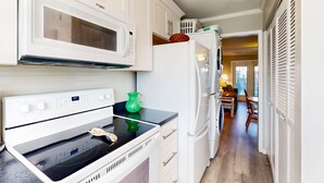 Una cocina con armarios blancos, microondas, estufa y refrigerador.