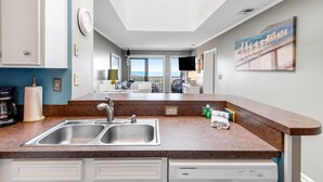 A modern kitchen with a double sink, built-in dishwasher, and a view to the living area. - 3rd Floor Oceanfront Condo w/Great Ocean and Pool Views and Shared Pools (Atlantic Beach)