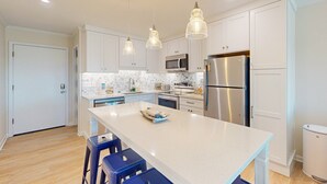 A modern kitchen with white cabinets, stainless steel appliances, and a central island with bar stools. - Condo with on-site beach access, pools, grill/picnic areas, & private balcony (Atlantic Beach)