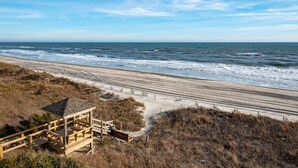 En strand med en trækonstruktion, en træpromenade og udsigt til havet.