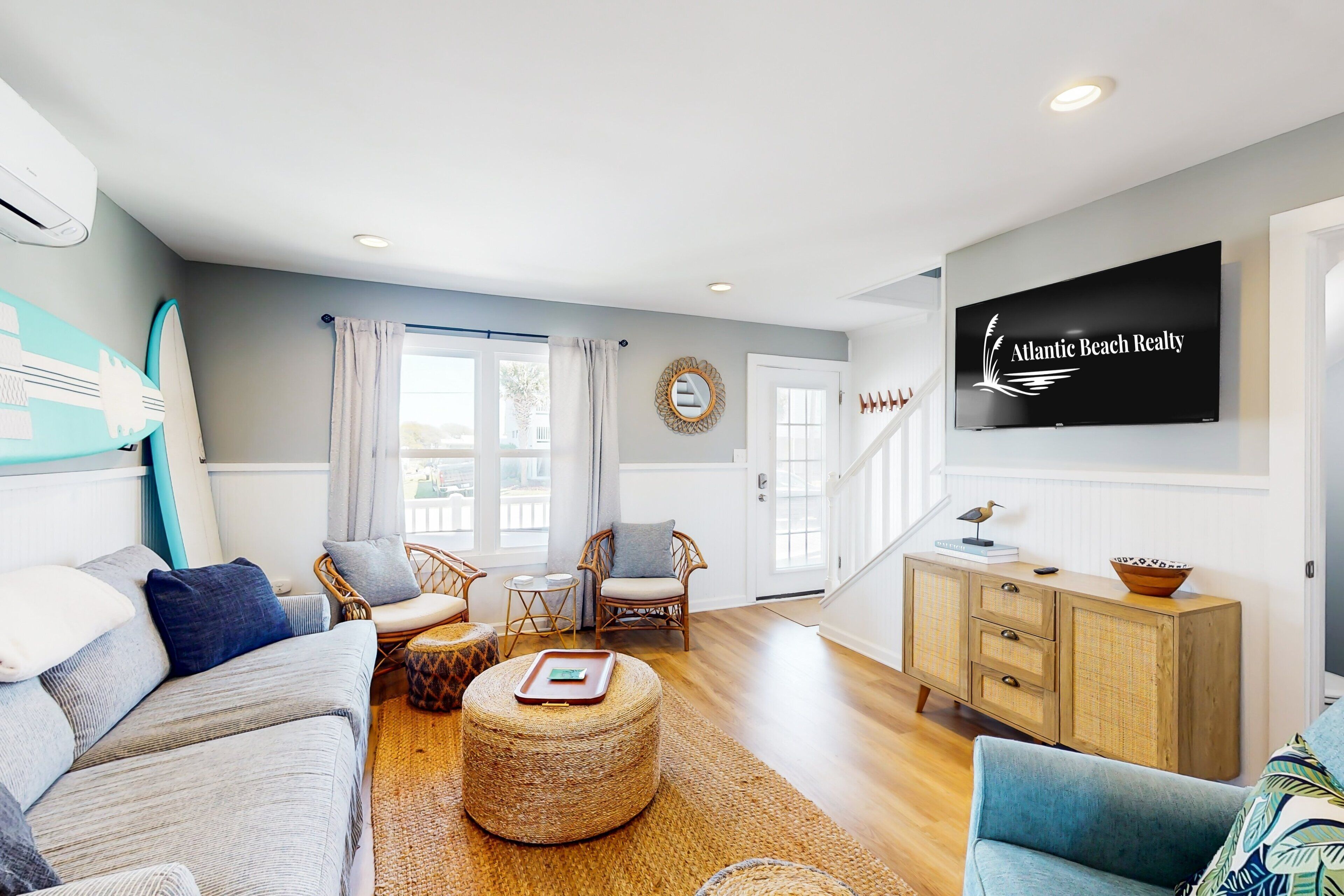 A modern living room with a sofa, ottoman, wicker chairs, a television, and a wooden cabinet.