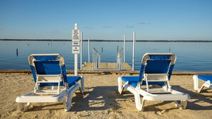 A beach with two blue and white lounge chairs facing the water, a pier, and a 'No Jumping or Diving' sign.