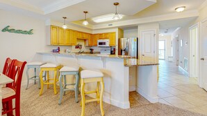A kitchen with a central island, yellow cabinets, and a 'beach' sign on the wall.