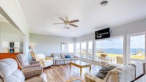 Tilava olohuone, jossa on suuri ikkuna, josta avautuu näkymä rannalle, kattotuuletin ja kyltti, jossa lukee Atlantic Beach Realty.