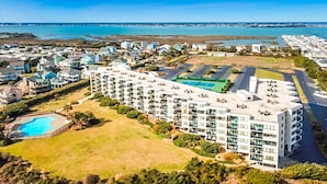 A multi-story hotel with a swimming pool, tennis courts, and a view of the sea.