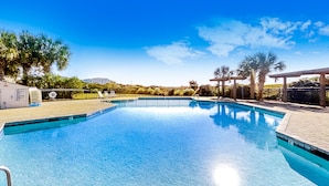 A clear blue swimming pool with a tiled deck, surrounded by palm trees and a covered seating area.