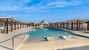 A swimming pool with lounge chairs and umbrellas, surrounded by covered areas and a building with a blue roof in the background. - The Gough Coast; 3BR with seasonal pool access & community dock (Beaufort)