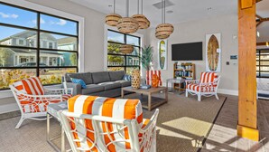 A spacious living room with large windows, wicker furniture, and a flat-screen TV. - The Gough Coast; 3BR with seasonal pool access & community dock (Beaufort)