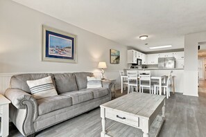 Un salon avec un canapé gris, une table basse et un coin repas avec des chaises blanches.