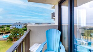 A balcony with a blue chair, a small table, and a view of a swimming pool and houses in the background.
