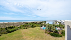 A residential area with a view of the beach, a swimming pool, and a grassy lawn.
