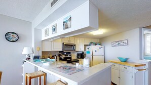 A kitchen with white cabinets, a central island with stools, a microwave, and a refrigerator.