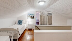 Un dormitorio con techo de madera, una cama con ropa de cama blanca, una mesita de noche y una ventana con contraventanas.